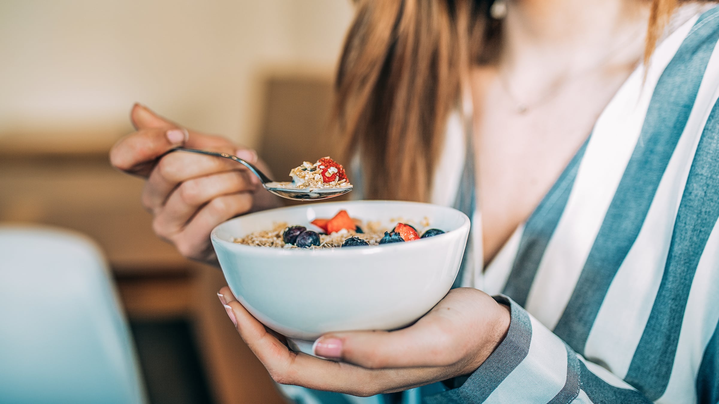 Crop woman close up eating oat and fruits bowl for breakfast Woman holding bowl of cereal with blueberries and strawberries