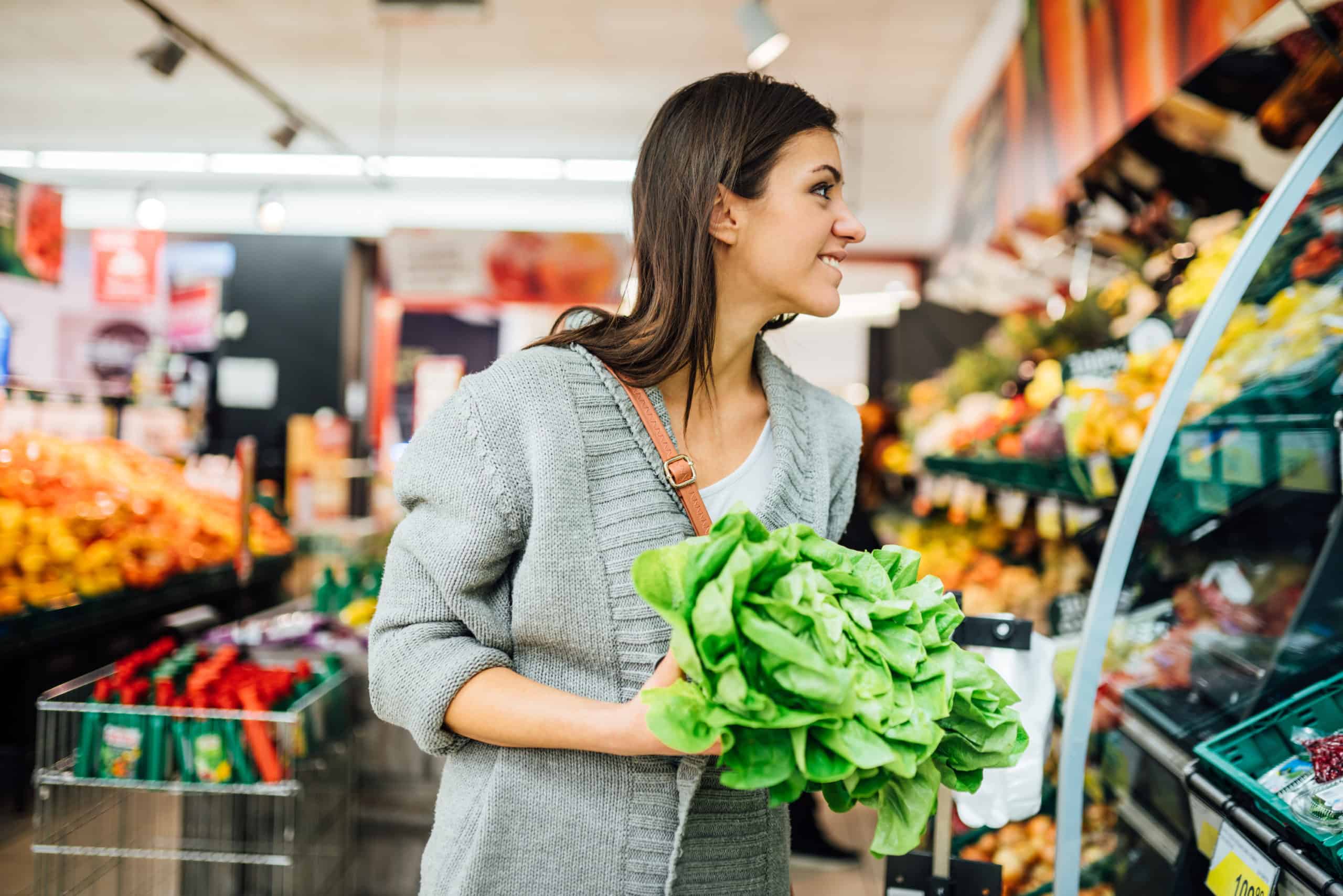 Young woman shopping in the supermarket grocery store for fresh greens.Buying organic vegetables sustainable produce.Natural source of vitamins and minerals.Vegan/vegetarian diet.Nutritional value Young woman holding lettuce in supermarket