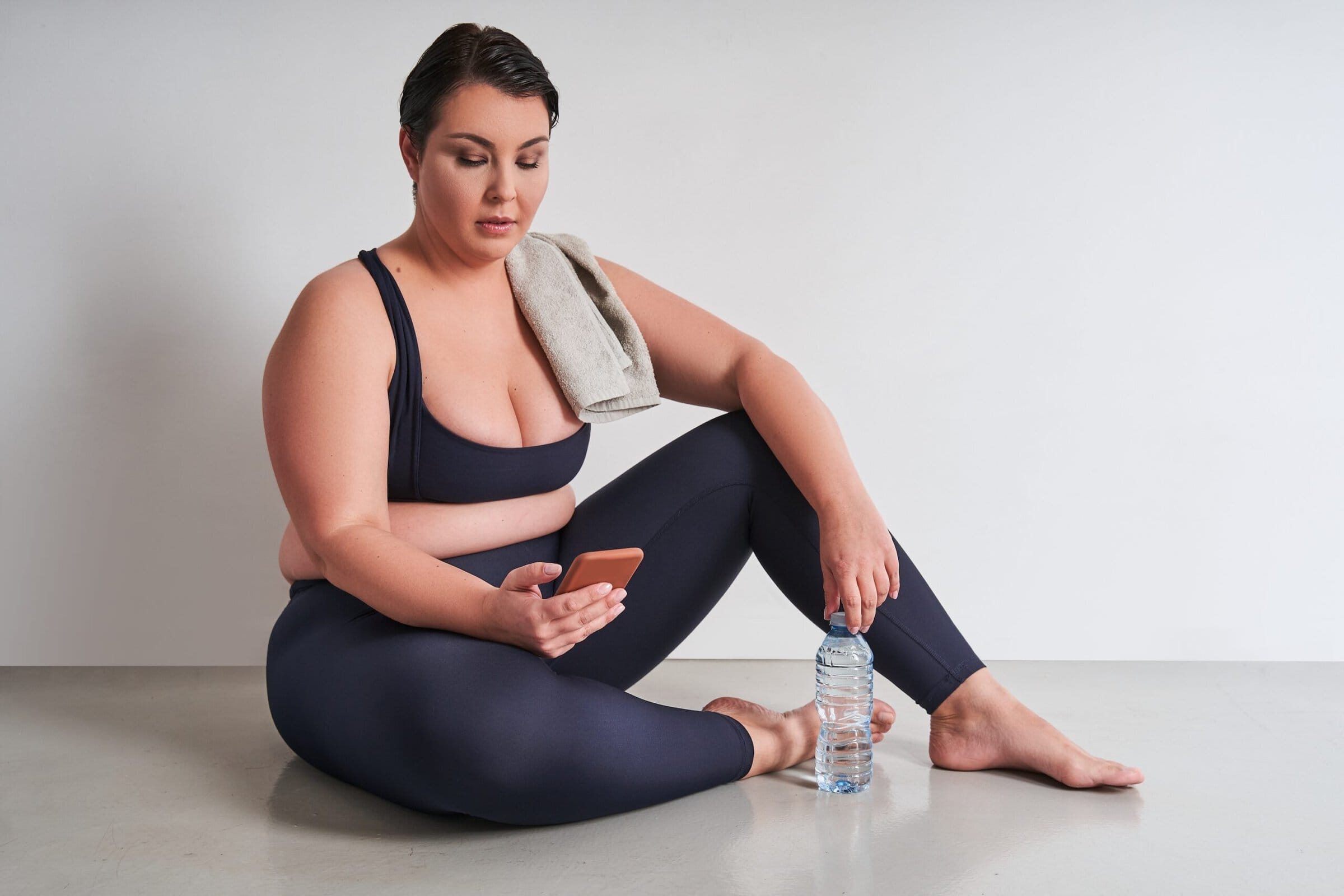 Plus,Size,Woman,Holding,Bottle,With,Water,And,Using,Smartphone